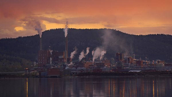 Sunset over the Domsjö plant against a forest backdrop and a river in the foreground. Sunset over the Domsjö plant against a forest backdrop and a river in the foreground.